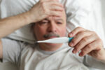 Older man sick in bed taking his temperature