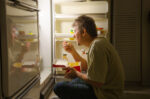 Man eating from refrigerator late at night