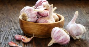 Bulbs of garlic in wooden bowl on table