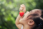 Happy young girl eating a strawberry
