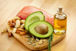 A selection of foods high in healthy fats, including salmon, avocado, olive oil and various nuts and seeds.