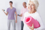 Older woman smiling with yoga mat