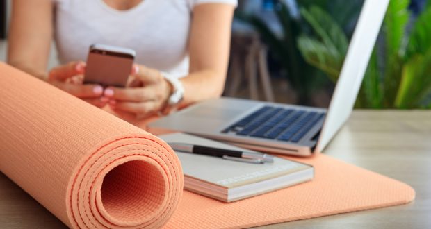 woman with cell phone, laptop, and yoga mat