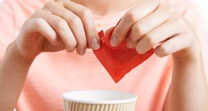 Woman adding artificial sweetener to coffee cup