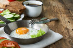 Fried egg in bowl with knife and fork on wooden table